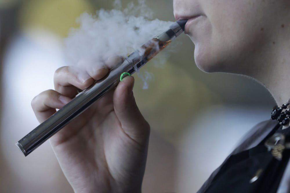 FILE - In this Friday, Oct. 4, 2019, file photo, a woman using an electronic cigarette exhales in Mayfield Heights, Ohio. A Michigan judge is blocking the state's two-week-old ban on flavored e-cigarettes. Court of Claims Judge Cynthia Stephens issued a preliminary injunction Tuesday, Oct. 15, 2019. She says Michigan Gov. Gretchen Whitmer's administration's delay in implementing the ban undercut its position that emergency rules were needed. (AP Photo/Tony Dejak, File)