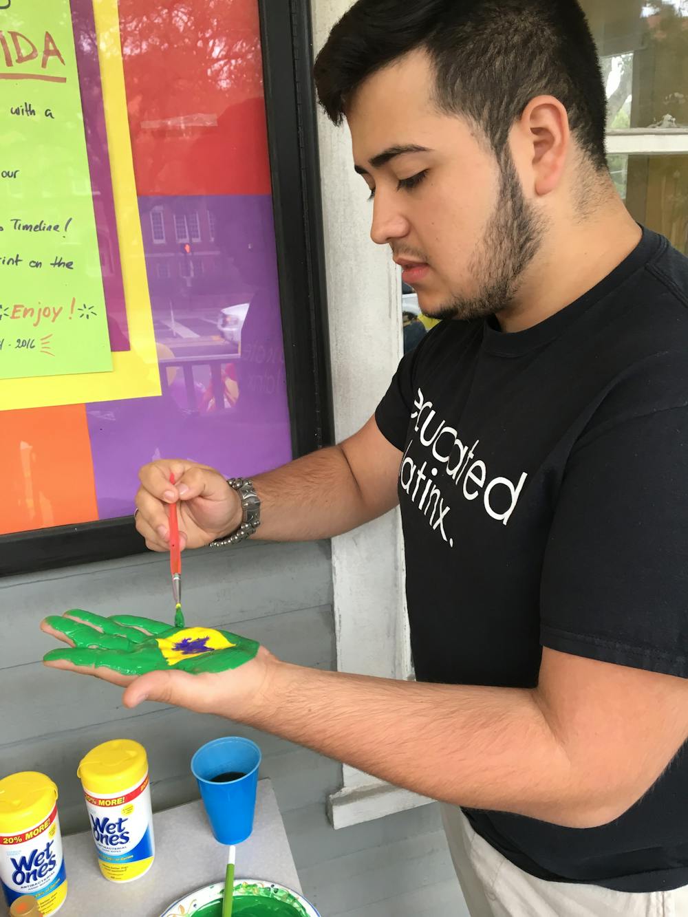 <p><span id="docs-internal-guid-149829e4-ed9f-f3fc-0bb9-9a7e8206168b"><span>Gabriel Costa, a 20-year-old UF music performance and nutrition sophomore, paints the flag of Brazil onto his hand to decorate the front of La Casita. Students left their handprints on the building as a final farewell.</span></span></p>