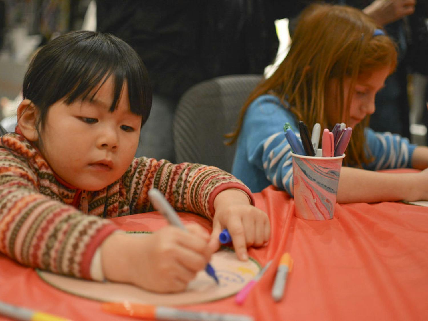 Nina Shou, 4, and Zoe Haller, 6, decorate fans with representatives from the Chinese Student Association at the Samuel P. Harn Museum of Art.