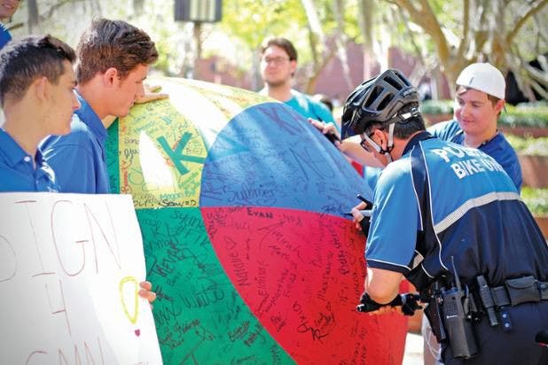 University Police officer, Henri Belleville, 43, signs a large beach volleyball during Zeta Beta Tau's grand debut philanthropy event. Every signature raises money for Children's Miracle Network Hospitals thanks to their sponsors.&nbsp;