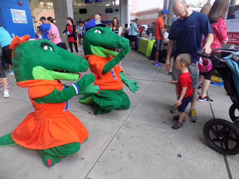 <p>Albert and Alberta show their Gator spirit by chomping and playing with a child before attendees started to run laps around Ben Hill Griffin Stadium.</p>