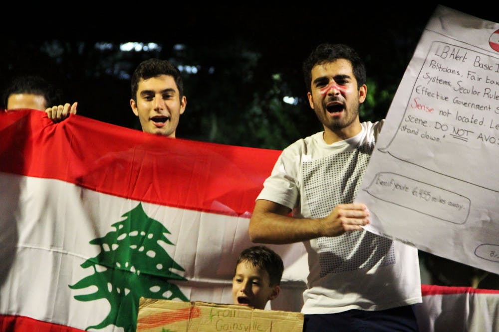 Michel Chalfoun, a 20-year-old computer science junior, and Malek Shehab, a 19-year-old industrial and systems engineering sophomore, hold the Lebanese flag and chant “Revolution!” in Arabic Tuesday night to stand in solidarity with the protestors in Lebanon. More than 40 people attended the protest.
