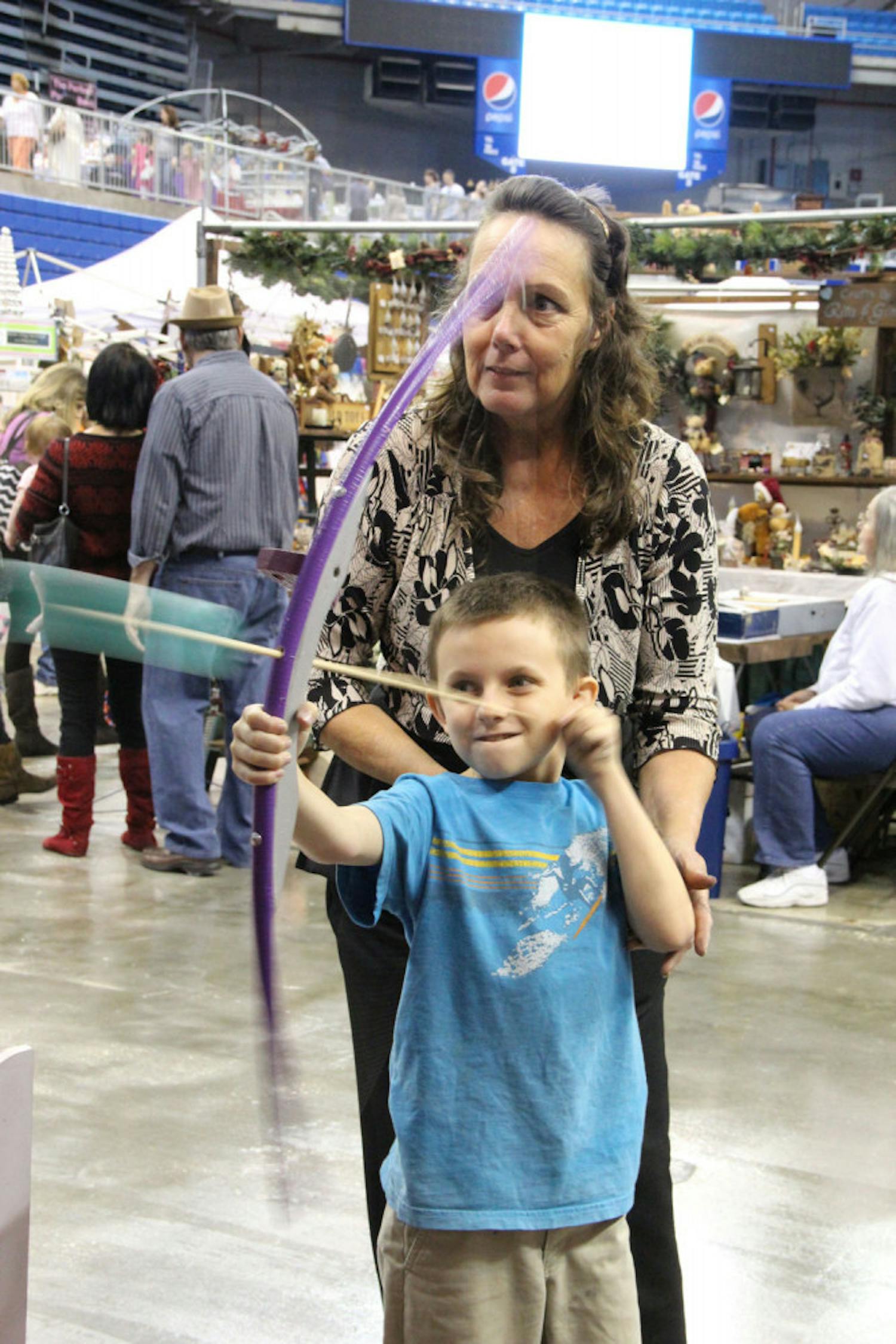 Jeanetta Scott, 58, shows Cayce Bowen, 8, how to shoot a bow and arrow at the 2015 Craft Festival. Scott is the owner of Jeanetta's Creative Designs alongside her husband, John Scott.