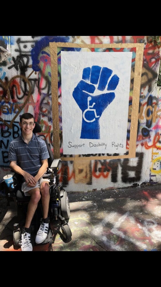 Bradley Minotti, a 21-year-old UF psychology junior who has had cerebral palsy since birth, sitting in front of a mural located in the Norman Tunnel that reads “Support Disability Rights.”