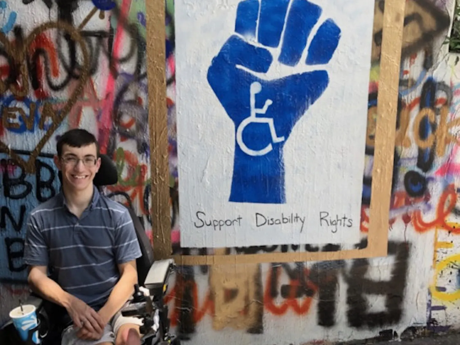Bradley Minotti, a 21-year-old UF psychology junior who has had cerebral palsy since birth, sitting in front of a mural located in the Norman Tunnel that reads “Support Disability Rights.”