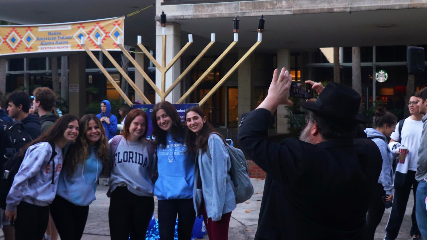Rabbi Berl Goldman takes a picture of a group of girls in front of the menorah at the Plaza of Americas on Monday, Nov. 29, 2021.