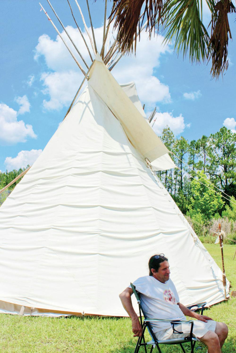 <p>Running Bear, owner of Running Bear’s Trading Post, sits outside of his tipi village at the Waldo Farmers and Flea Market Sunday. The tipis are decorated with traditional Native American items.</p>