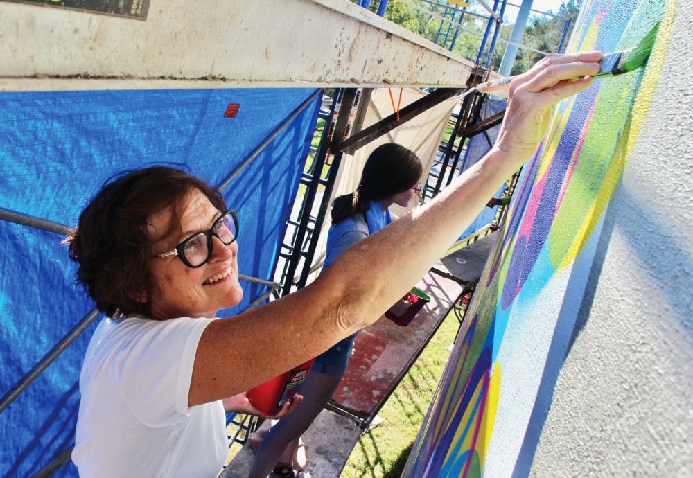 Julia Morrisroe, 55, an associate professor of painting and drawing works on a public art mural along with Laura North, 23, UF fine arts senior, called "Currents of Data,” which stemmed from the Creative B program. The mural is being painted on the Water Reclamation Tank located on Gale Lemerand Drive.