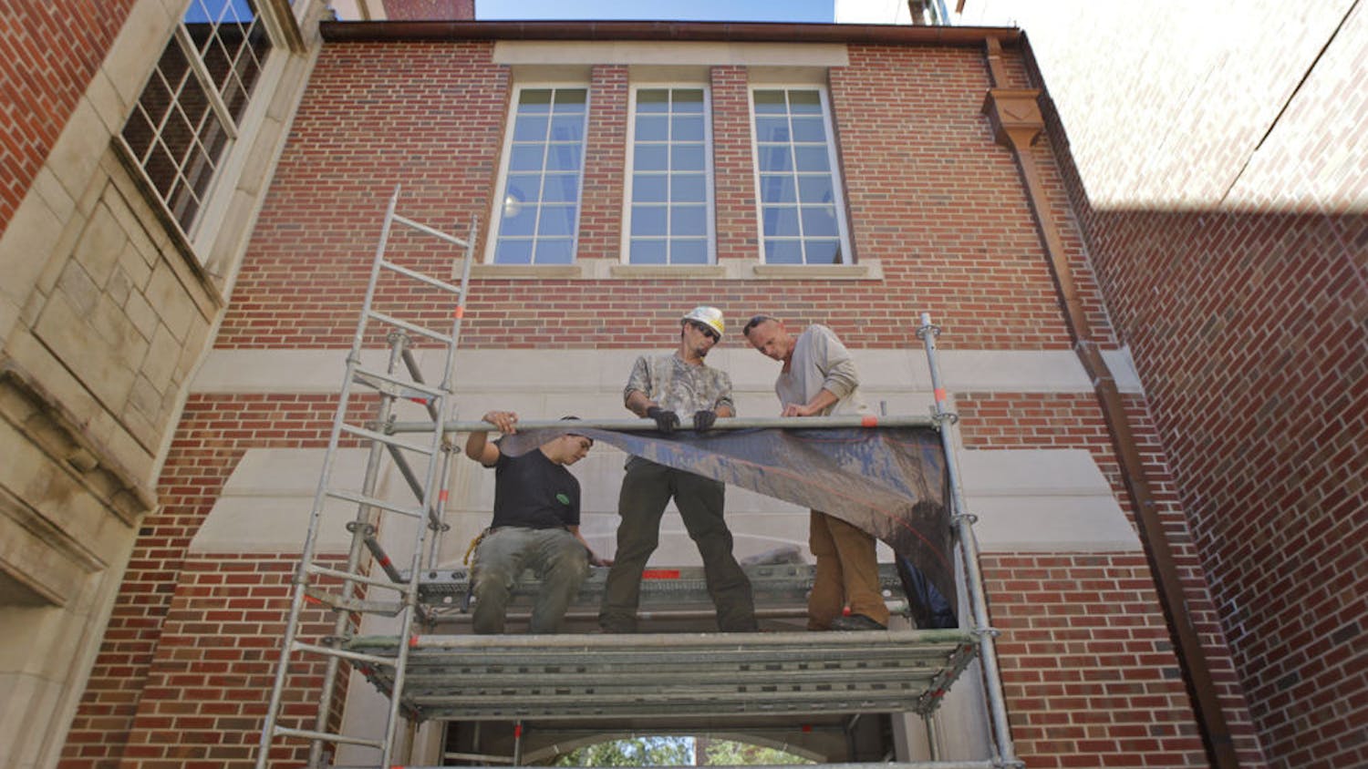 From left: Custom Quality Scaffold builders Bryson Swails, Dan Yunk and Chuck Griffith set up to work on the double archway at Heavener Hall. Three secular quotations will be added to the archway to supplement the Bible verse already inscribed on it.