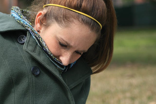 Rhianna Reed, 22-year-old food and resource economics senior, uses her scarf and coat to stay warm while studying in the grass behind The Hub on Monday afternoon.