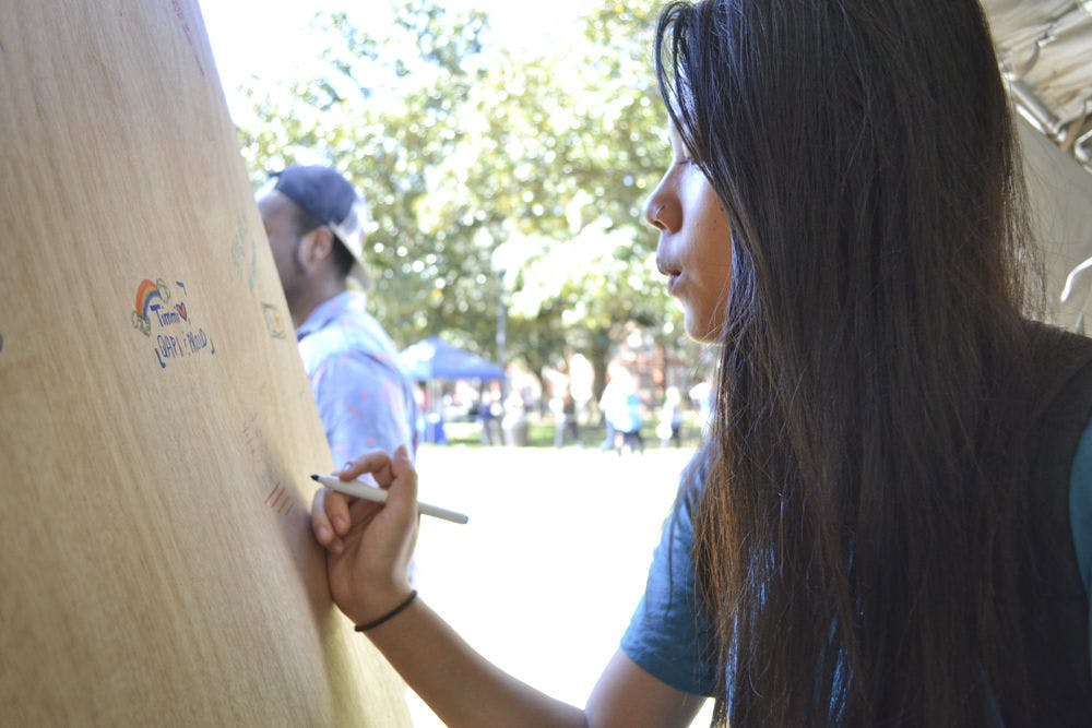 <p>Natalie Heller, a 20-year-old finance junior, writes her name on the door at National Coming Out Day on the Plaza of the Americas on Oct. 12, 2015, to support coming out. Heller said writing her name on the door meant not being afraid. “If someone were to walk by and see my name, I wouldn’t care,” Heller said. “The same time last year I wouldn’t have been willing to.”</p>
