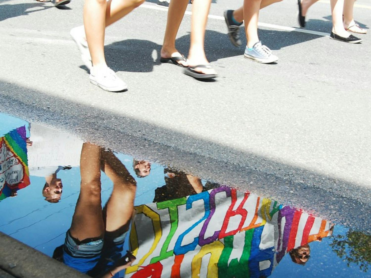 Festival attendees hold up rainbow signs in support of the Gainesville Pride Festival and Parade, as seen through a reflection on the road on Saturday. The festival celebrates people of all different sexual orientations and allows them to share their pride with everyone.