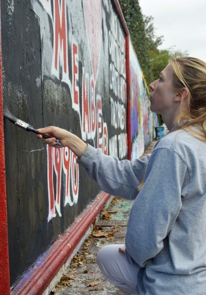 Brianna Rubel, 25, restores a memorial for the victims of the Danny Rolling murders on the 34th Street Wall. She decided to help another artist paint over hateful comments in the “remember” section Tuesday.