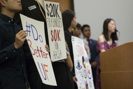 Khanh Hoang, 20, holds a protest sign alongside other protesters while Wenxin Song speaks during a Student Government Senate meeting in the Reitz chamber room Tuesday evening. Song is the Internal Vice President for the Korean Undergraduate Student Association. “It’s more than just a show,” Song said. “It is our tradition and our legacy here.”