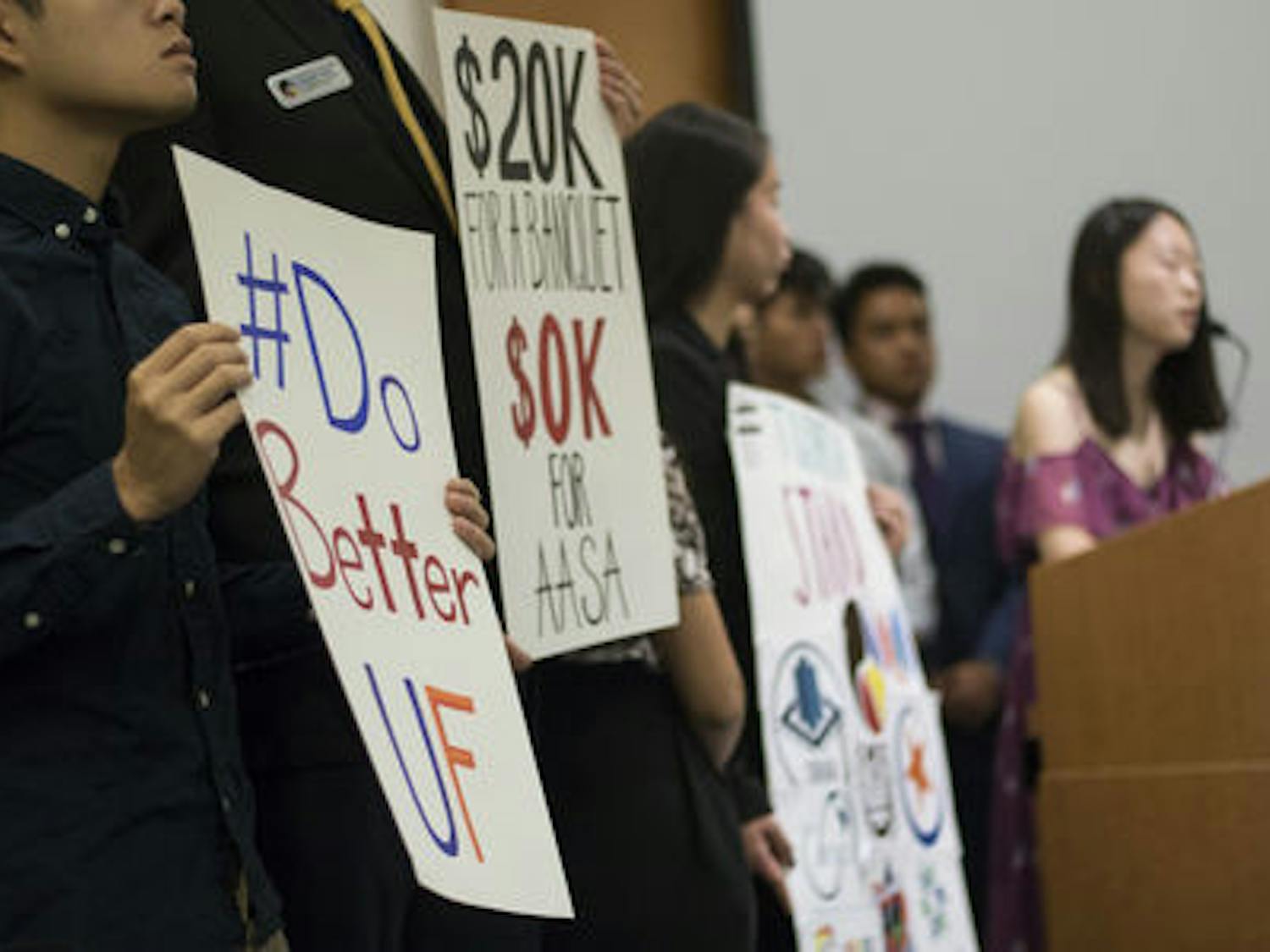 Khanh Hoang, 20, holds a protest sign alongside other protesters while Wenxin Song speaks during a Student Government Senate meeting in the Reitz chamber room Tuesday evening. Song is the Internal Vice President for the Korean Undergraduate Student Association. “It’s more than just a show,” Song said. “It is our tradition and our legacy here.”