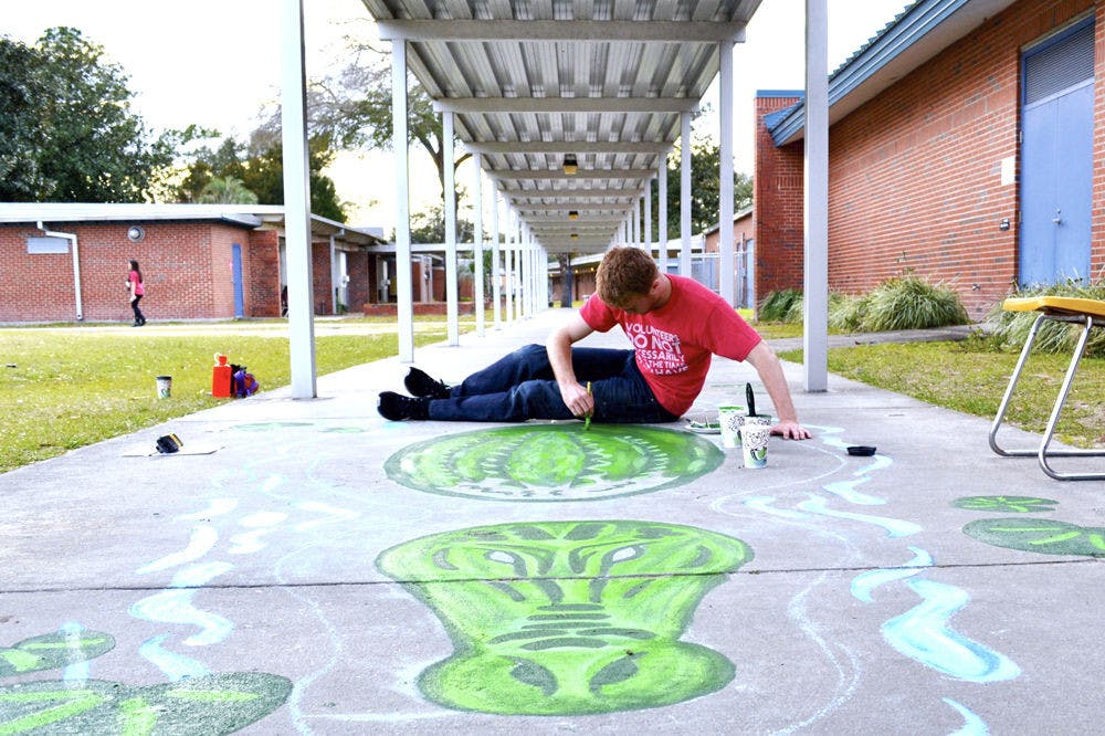 Brandon Peebles, 21, an art coordinator for Project Makeover, paints an alligator on the sidewalk at W.A. Metcalfe Elementary School. Members and volunteers painted murals all around the school, including musical instruments in the music room, a Dr. Seuss themed kindergarten area and an ocean scene in the cafeteria.