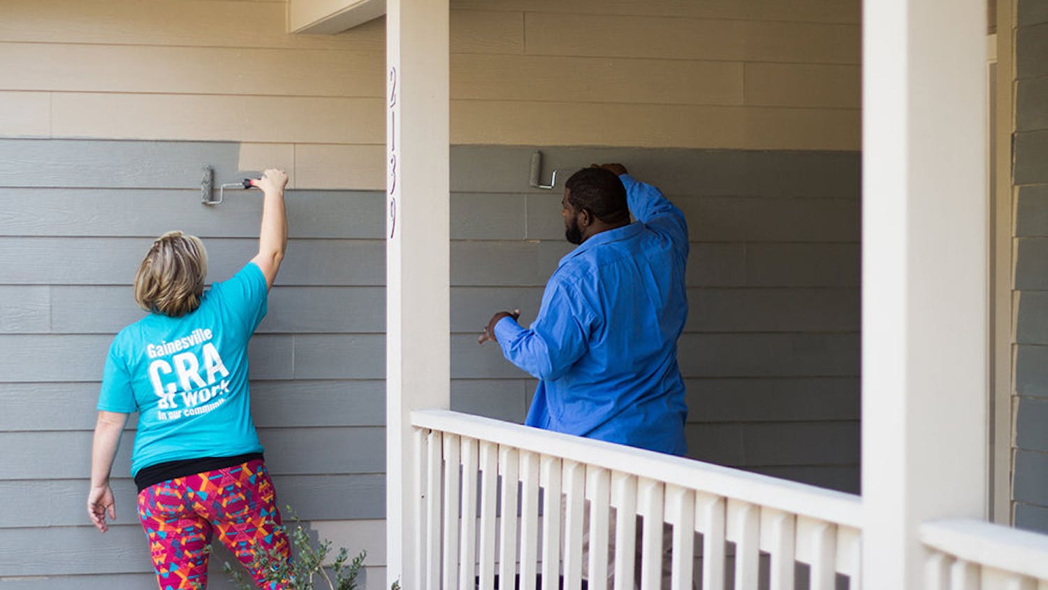 Two people paint a Gainesville residence gray. The Gainesville Community Redevelopment Agency's residential paint program helps local residents with pressure washing and painting costs. 