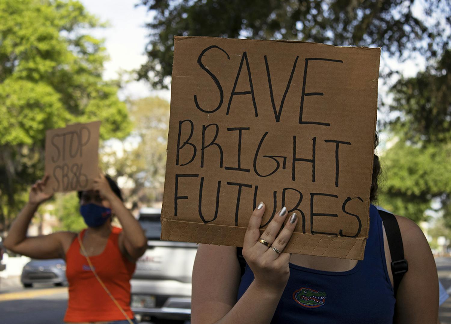 Aleidys Lopez (right), 19, a sustainability studies and women's studies sophomore shields her face from the sun with a "Save Bright Futures" sign as she and three other protestors march down University Avenue on Friday, March 26, 2021. The protest was held to raise awareness about Senate Bill 86, which was amended on Tuesday.