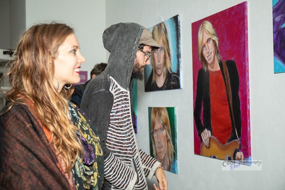 <p>Two attendees at Friday night's reception for the Matheson's new Tom Petty exhibit look at paintings of the musician created by local artist Barbara Tench.</p>