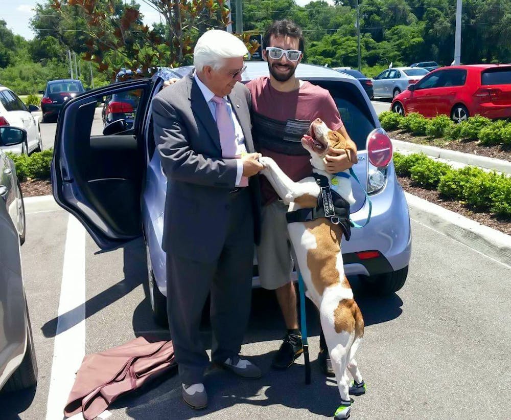 <p>Ty Redler (center), with his dog Rusty, shaking hands with Don, a salesman at an Ocala Volkswagen dealership. “When I bought my car I brought rusty with me so that’s rusty sealing the deal (sic),” Redler wrote in a text message.</p>