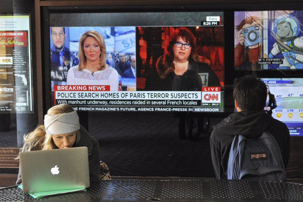 Hannah Bodem, a 22-year-old UF telecommunication senior, reviews her class schedule on her computer in the Weimer Hall atrium on Thursday. Behind her, the television display shows the latest developments in the Charlie Hebdo case.