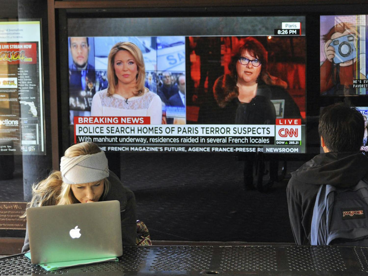 Hannah Bodem, a 22-year-old UF telecommunication senior, reviews her class schedule on her computer in the Weimer Hall atrium on Thursday. Behind her, the television display shows the latest developments in the Charlie Hebdo case.