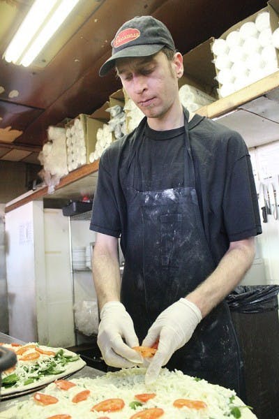 Edgar Hathaway, shift manager at Leonardo’s Pizza by the Slice, puts tomatoes on a pizza in 2010.