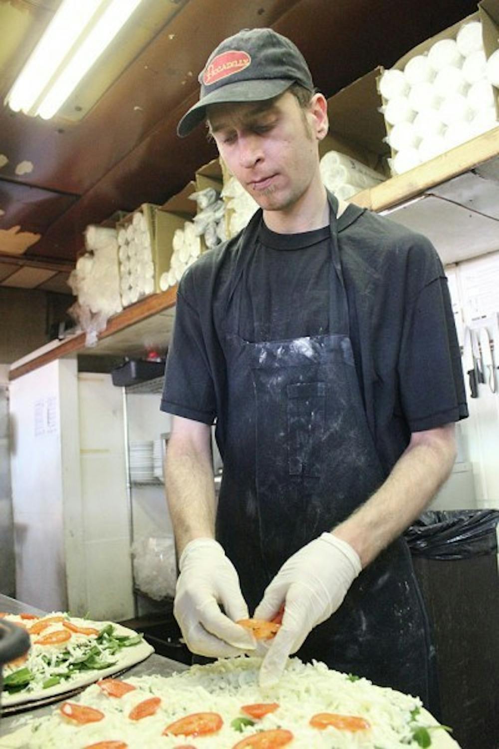 <p>Edgar Hathaway, shift manager at Leonardo’s Pizza by the Slice, puts tomatoes on a pizza in 2010.</p>