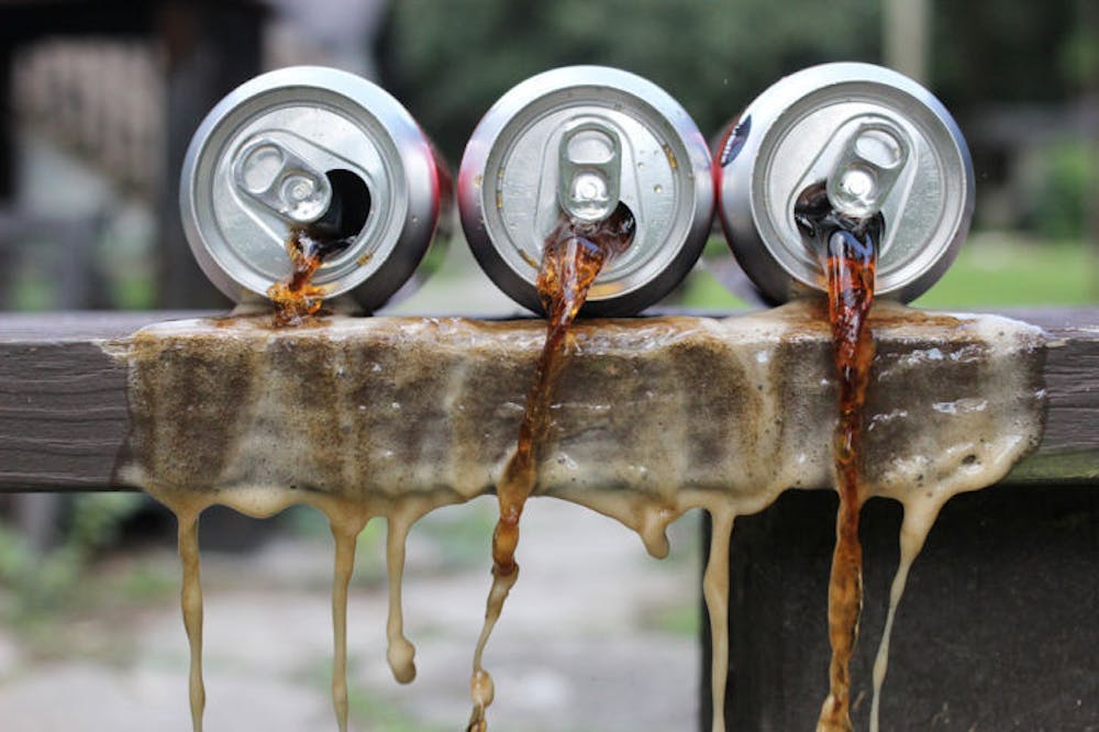<p>A set-up photo shows soda spilling out of cans. A recently published study suggests that the alertness experienced after drinking sugary beverages is actually more of a placebo effect than the effect of the sugar.</p>