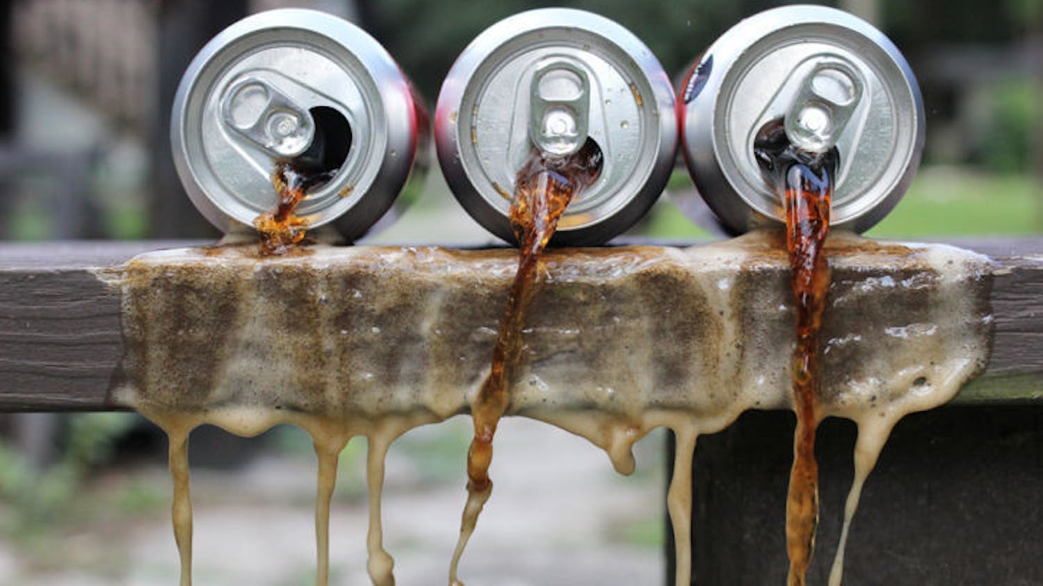 A set-up photo shows soda spilling out of cans. A recently published study suggests that the alertness experienced after drinking sugary beverages is actually more of a placebo effect than the effect of the sugar.