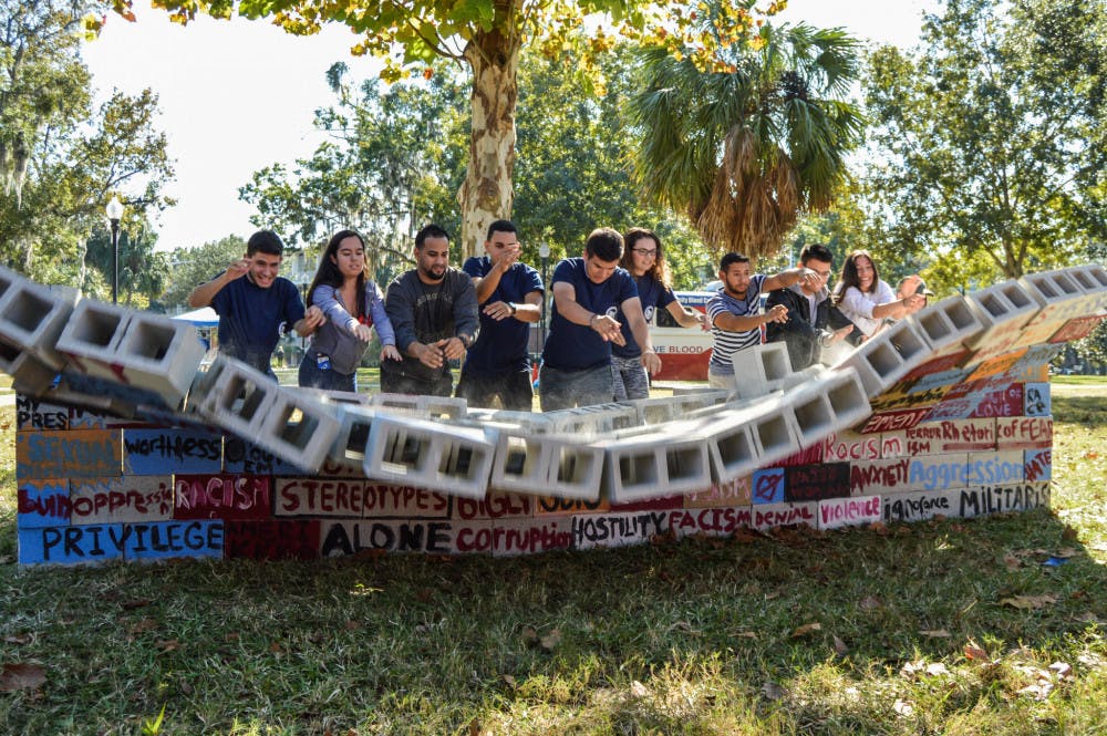 The UF Hispanic Student Association and Hispanic-Latino Affairs break down a wall made of cinder blocks for a unity demonstration behind the Hub on Thursday afternoon. Throughout the day, the organizations invited students to write words and phrases they found harsh and cruel, with the intent to tear them down.