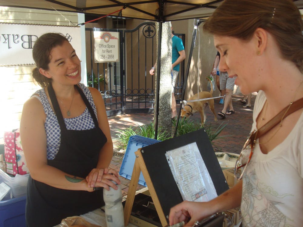 <p>Erin Carlson, 22, stops at Amanda Bowers’ table of goods from her bakeshop BakerBaker for a pecan bar. Carlson was meandering through Haile Farmers Market that winds through Haile Village Saturday.</p>