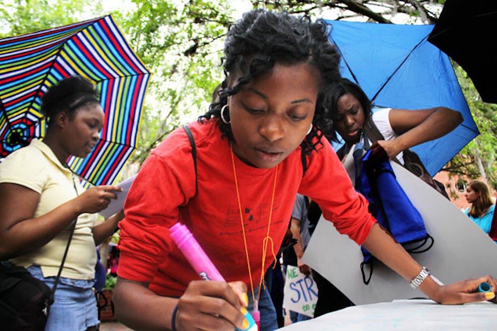 <p>Criminology senior Charkivia Lovett, 22, makes a sign that reads "We are women, we are men. Together we fight to take back the night." at the Take Back the Night rally on Wednesday to fight against sexual violence.</p>