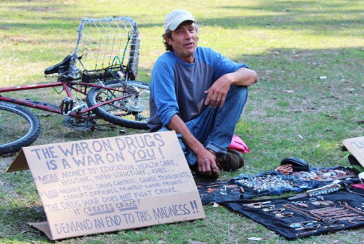 David Erickson, also known as D. Sinn, sits on the lawn on Plaza of the Americas on Monday afternoon. His art exhibit is titled Living Art in America. Erickson is often found around campus selling knickknacks to students passing through the plaza.