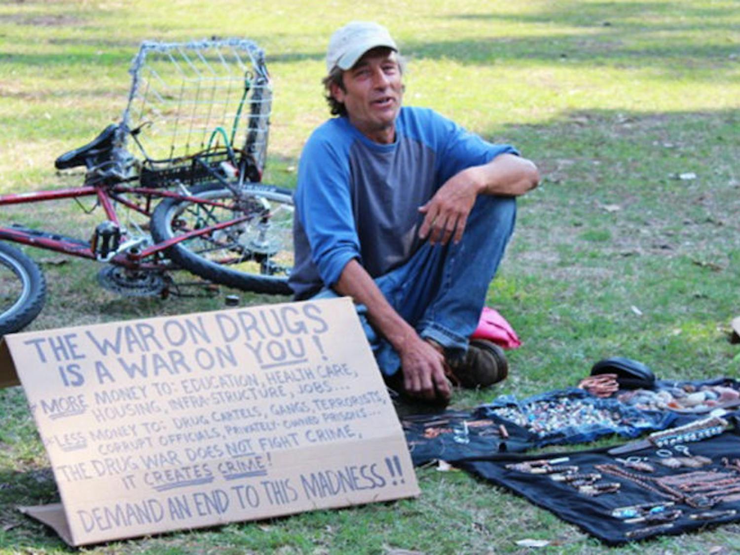 David Erickson, also known as D. Sinn, sits on the lawn on Plaza of the Americas on Monday afternoon. His art exhibit is titled Living Art in America. Erickson is often found around campus selling knickknacks to students passing through the plaza.