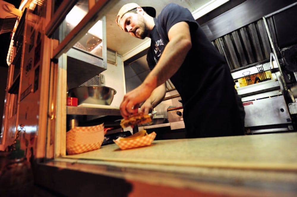 <p>Mike Riska, 30, of the Pelican Brothers food truck serves up a “Ghetto Burger” to a customer at the truck’s late-night regular spot, the parking lot of High Dive in downtown Gainesville, Tuesday night.</p>
