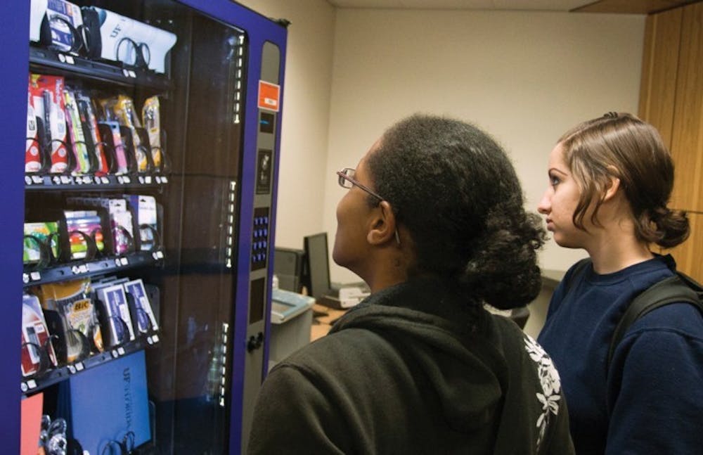 <p>Psychology senior Jodi Wallace and biology senior Noelani Arango look at the inventory in the school-supply vending machine, located on the second floor of Library West on Tuesday afternoon.</p>