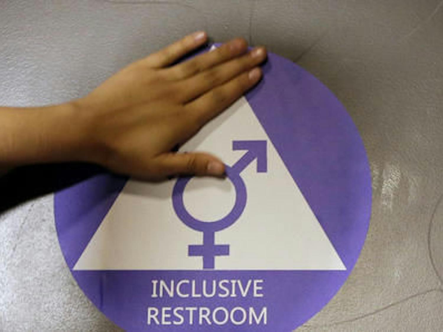 In this May 17, 2016 file photo, a new sticker is placed on the door at the ceremonial opening of a gender neutral bathroom at Nathan Hale High School in Seattle. A government official says the Trump administration will revoke guidelines that say transgender students should be allowed to use bathrooms and locker rooms matching their chosen gender identity.