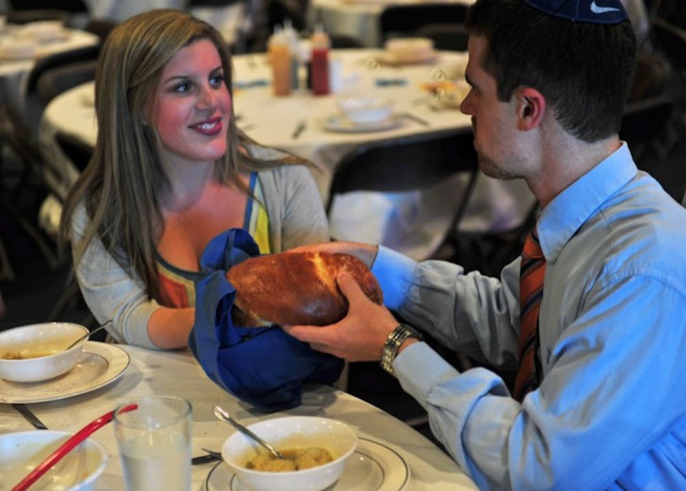 <p>Brooke Schwartzman and Adam Firestone pass challah bread around the table during the pre-fast dinner for Yom Kippur at UF Hillel Tuesday night.</p>