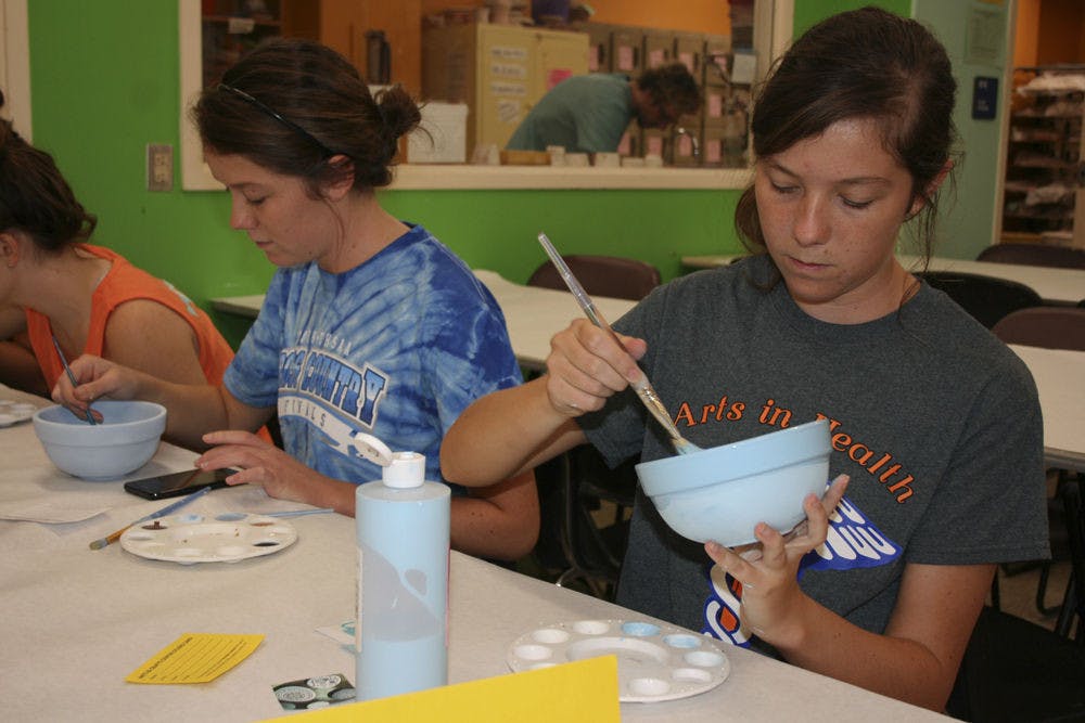 Twins Kayla and Sarah Miller, both 21-year-old UF health science pre-occupational therapy and nursing seniors, paint bowls with the Arts in Health Club to help raise money for St. Francis House.