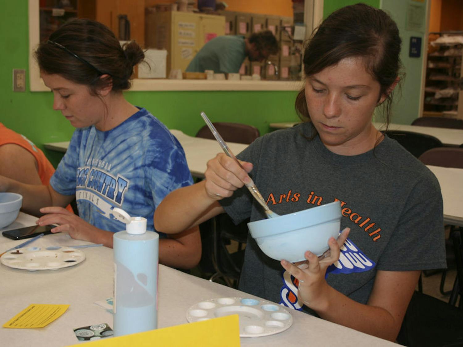 Twins Kayla and Sarah Miller, both 21-year-old UF health science pre-occupational therapy and nursing seniors, paint bowls with the Arts in Health Club to help raise money for St. Francis House.