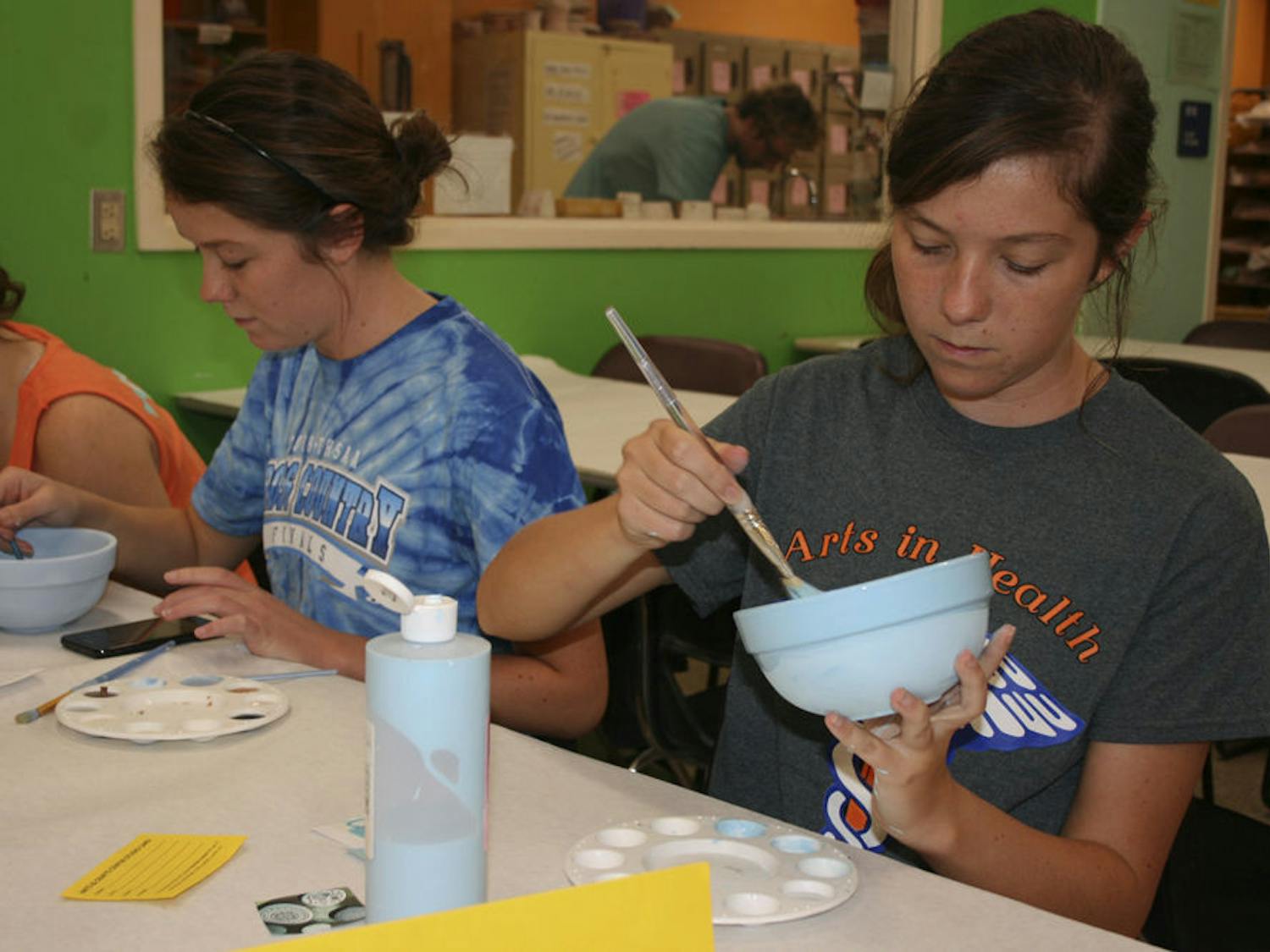Twins Kayla and Sarah Miller, both 21-year-old UF health science pre-occupational therapy and nursing seniors, paint bowls with the Arts in Health Club to help raise money for St. Francis House.