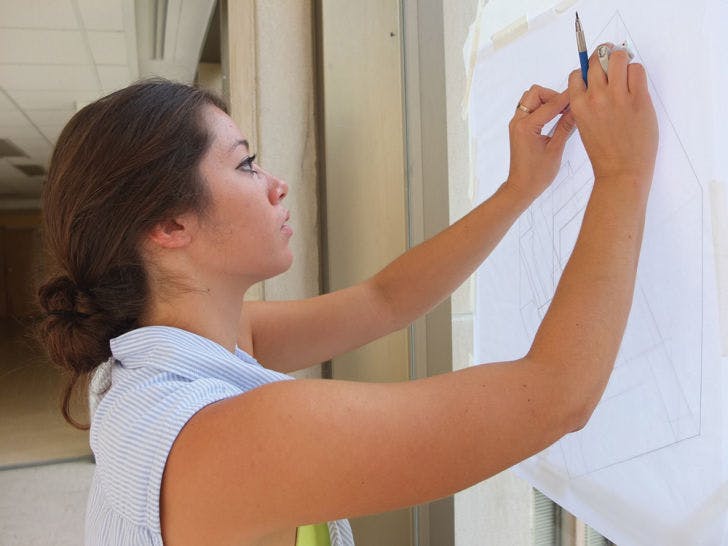 Nikki Yager, 18, works on a sketch of a cube Tuesday morning. The freshman architecture major used the windows in the overpass between Fine Arts Buildings A and C in lieu of a light box.