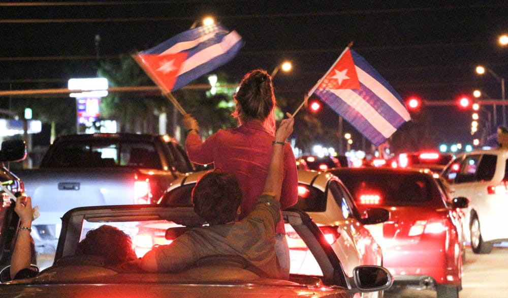 Two people wave Cuban flags as they are driven down Bird Road in Miami on Saturday night. People were either passing by or parking at La Carreta, a Cuban restaurant, to celebrate and cheer on the death of former Cuban leader Fidel Castro.