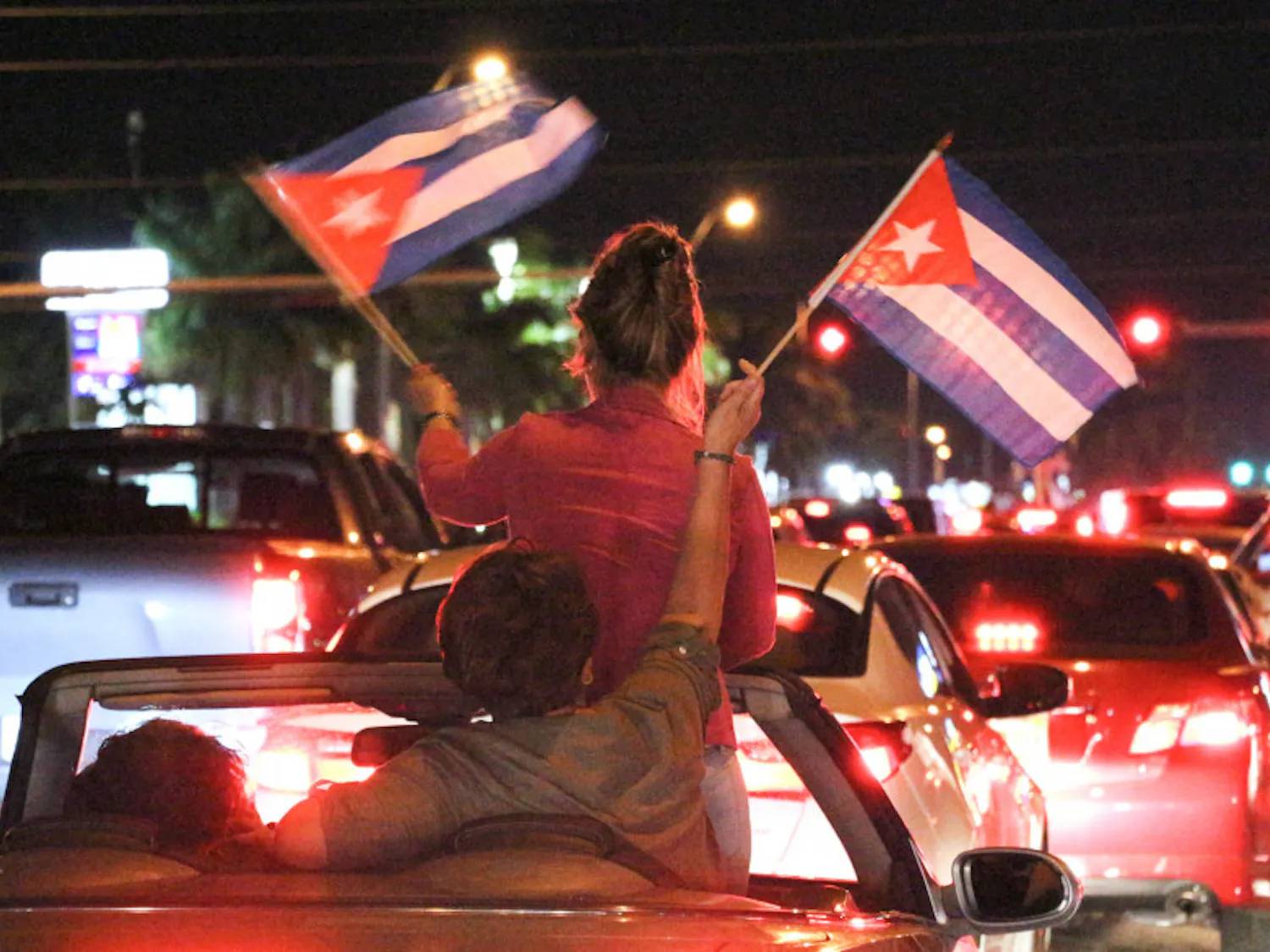 Two people wave Cuban flags as they are driven down Bird Road in Miami on Saturday night. People were either passing by or parking at La Carreta, a Cuban restaurant, to celebrate and cheer on the death of former Cuban leader Fidel Castro.