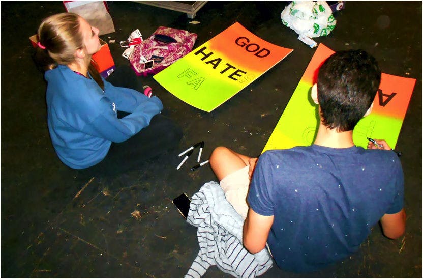 Stephanie Watson, 19, and Matthew Henao, 20, make protest signs that will be used for props in "Thank God for AIDS." The play premieres Friday.