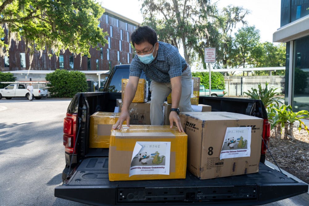 Changweng Deng, one of the donation organizers, unloads boxes of PPE from the back of a pickup truck on Thursday to donate to UF Health Shands Hospital. Everyone present at the donation observed social distancing guidelines by standing six feet apart and wearing facemasks to protect themselves from COVID-19, they told The Alligator.