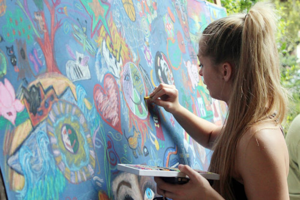 <p class="p1"><span class="s1">Coral Hawking, a 19-year-old UF applied physiology and kinesiology freshman, colors on a blue bed sheet as part of Paul Wislotski’s collective art project outside Gator Corner Dining Center on Sunday afternoon. Wislotski is trying to hitchhike to at least two universities in every state.</span></p>