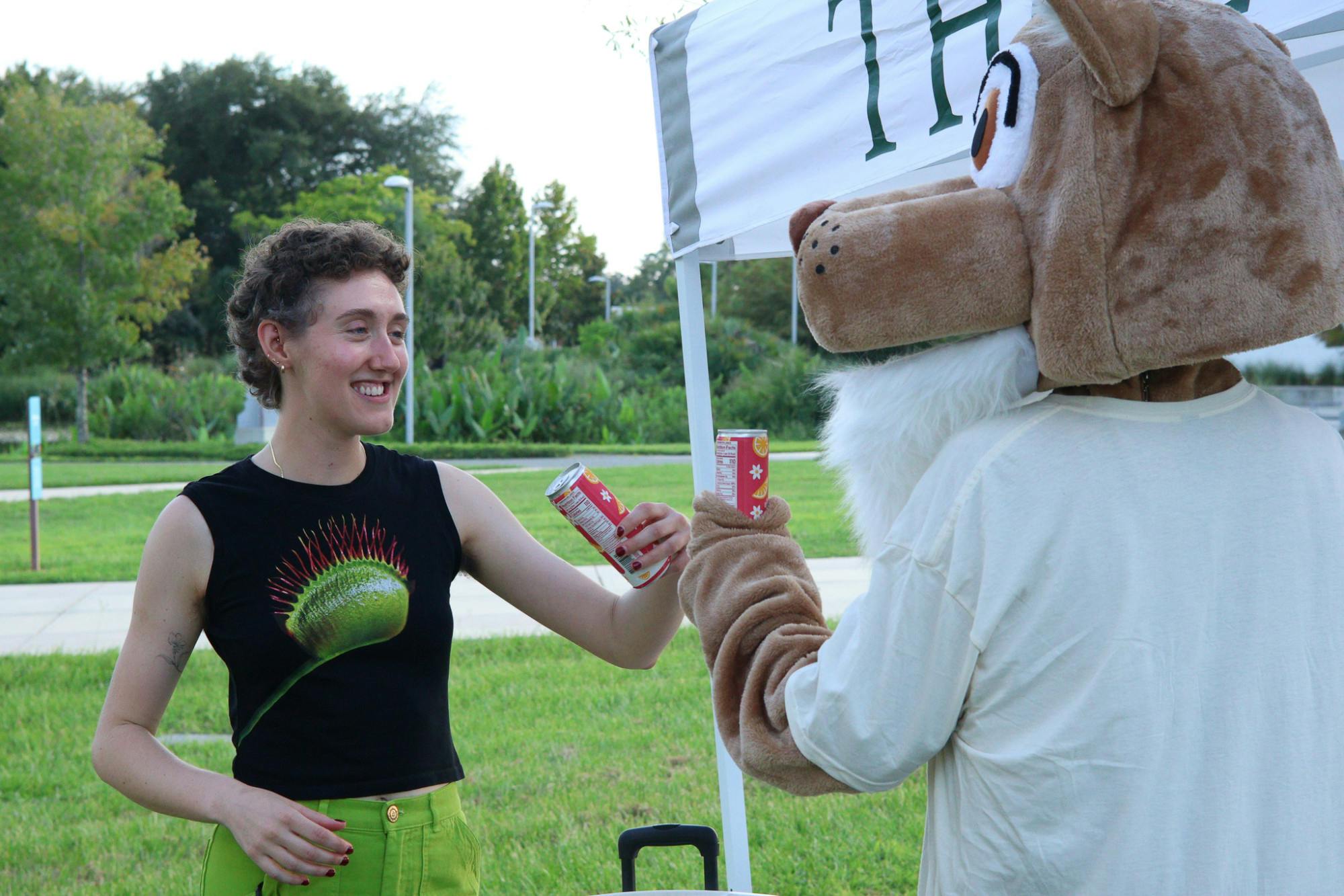 A mascot for The Lynx Books enjoys a fizzy drink with Viv Schnabel, a 25-year-old event coordinator, at the bookstore's Gainesville Reads kickoff event at Depot Park Monday, Sept. 1.