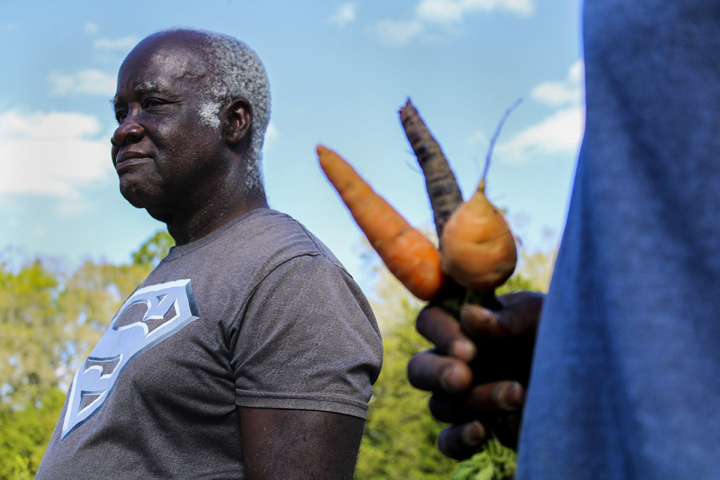 Lennon Fisher Jr. holds three different kinds of carrots in his hand while Lennon Fisher looks at the field. They said some of their favorite produce are their carrots.